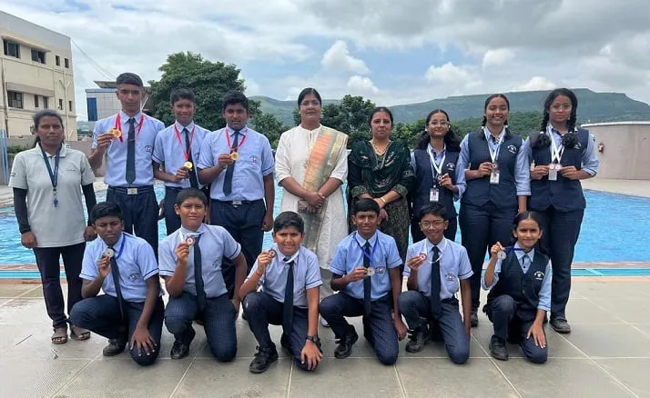 A group of students in blazers wearing medals beside the pool
