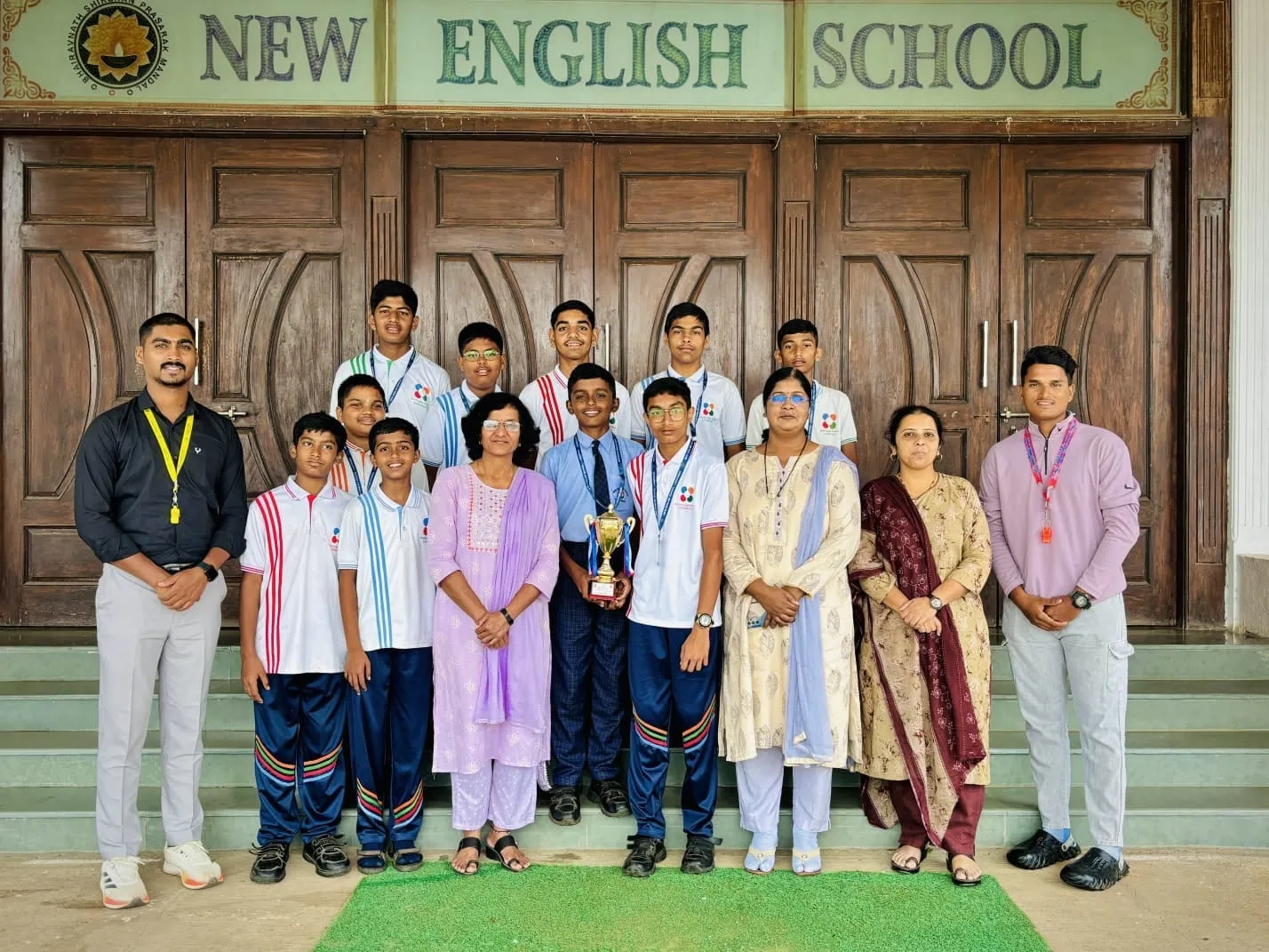 NES students and teachers holding a trophy in front of the school doors