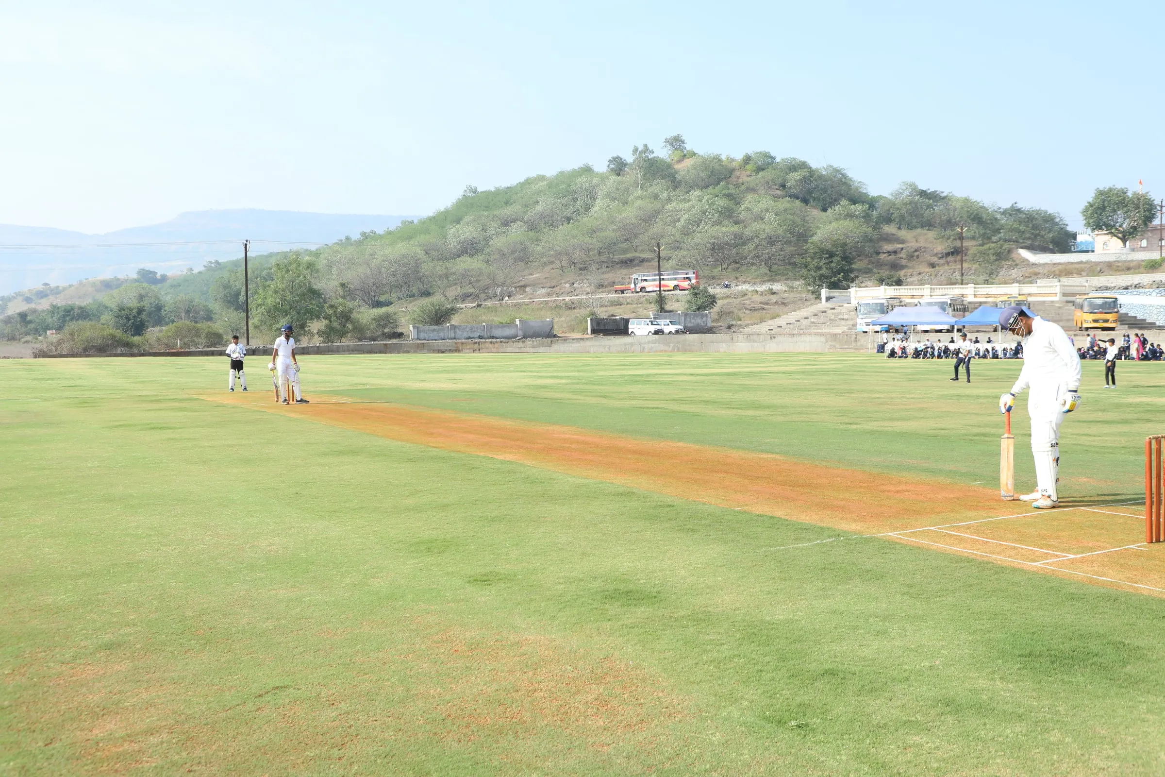 A cricket match on the green ground below a hill