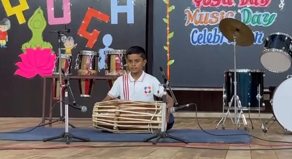 A student playing a dholki on stage at the Music Day celebration