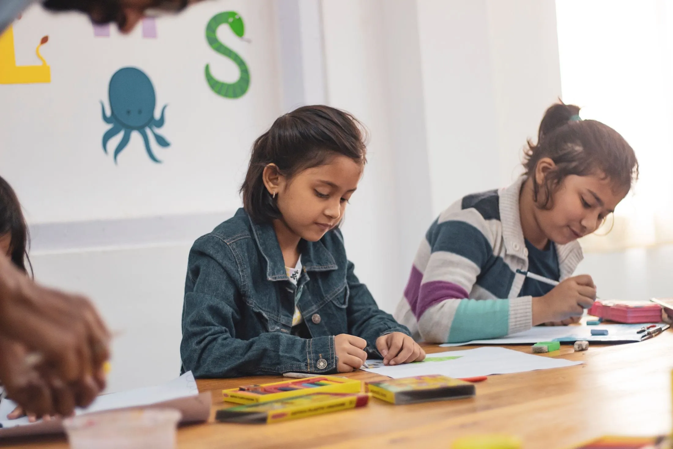 Two young girls drawing with crayons at a classroom table
