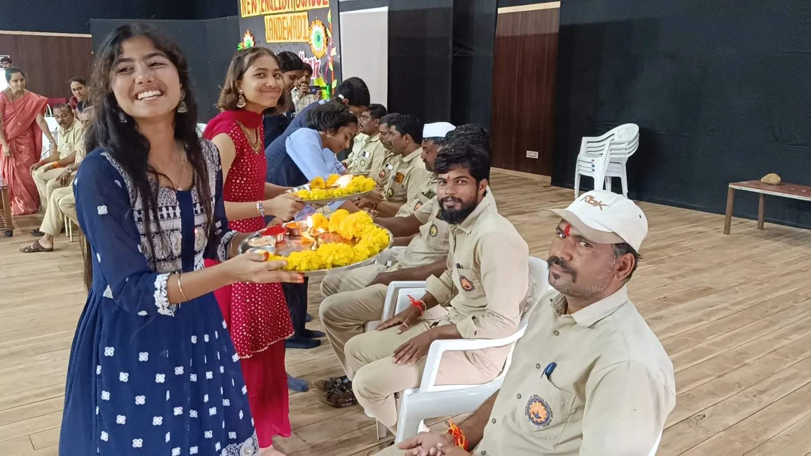 A smiling student holding a plate of marigolds for Raksha Bandhan beside the campus security staff
