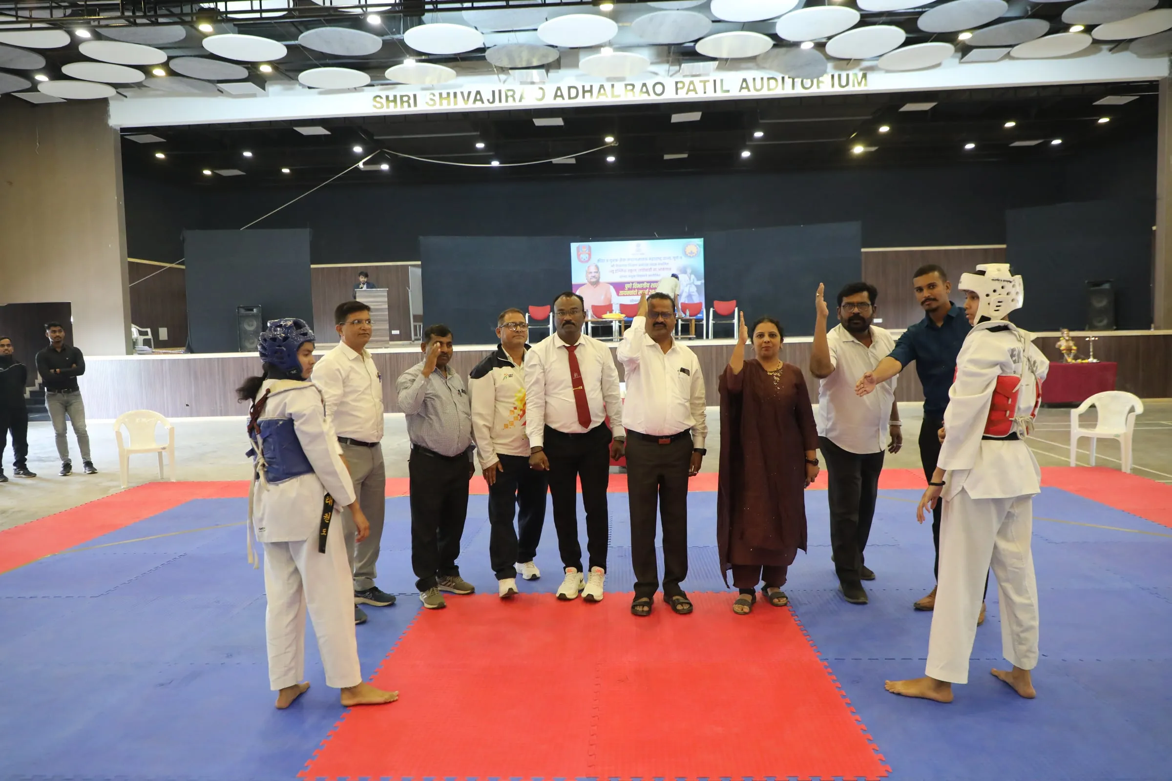 Two taekwondo players in protective gear with officials in the auditorium
